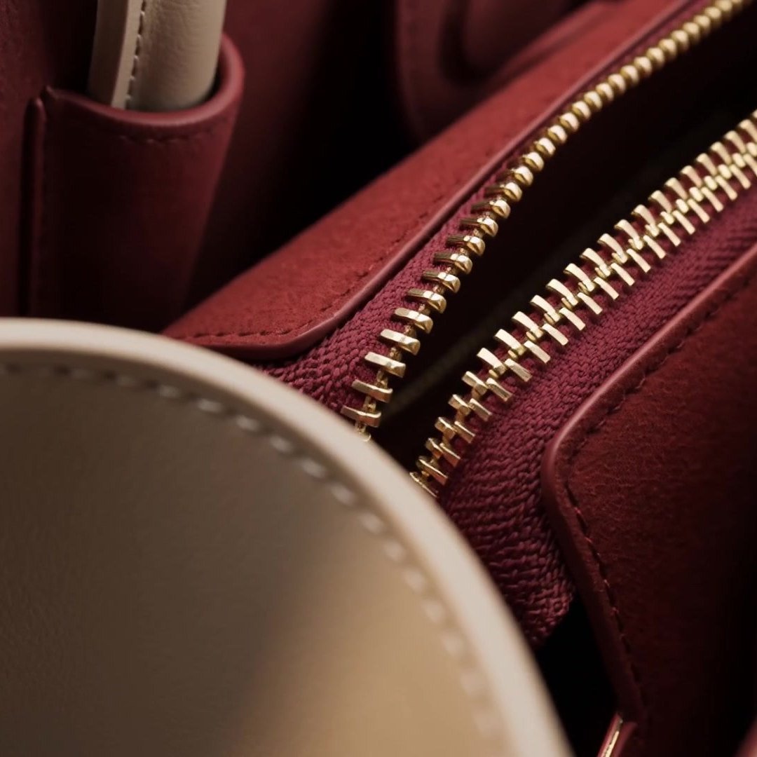 A gold-tone zip pull against the dark burgundy suede interior.