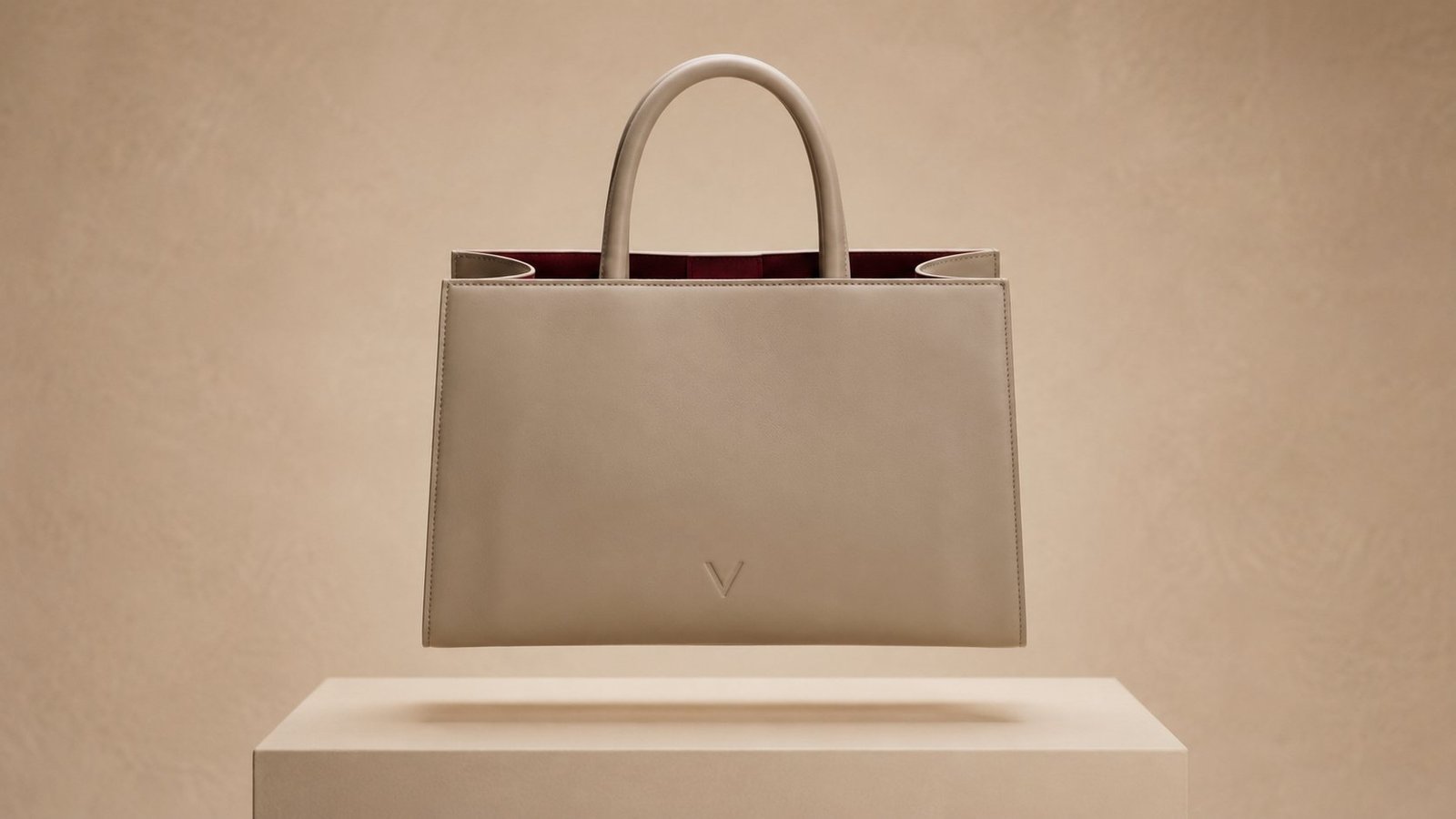 The Élan tote seen straight on, suspended above a pale plinth, the front panel unbroken but for a small blind-embossed mark.