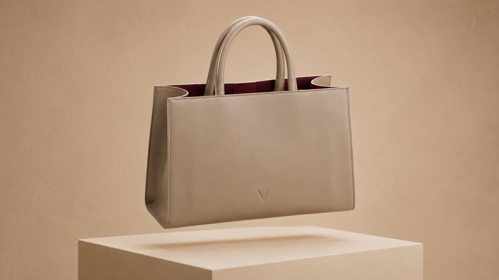 Three-quarter view from the left showing the taupe cowhide panel meeting the side gusset, with dark burgundy visible at the opening.