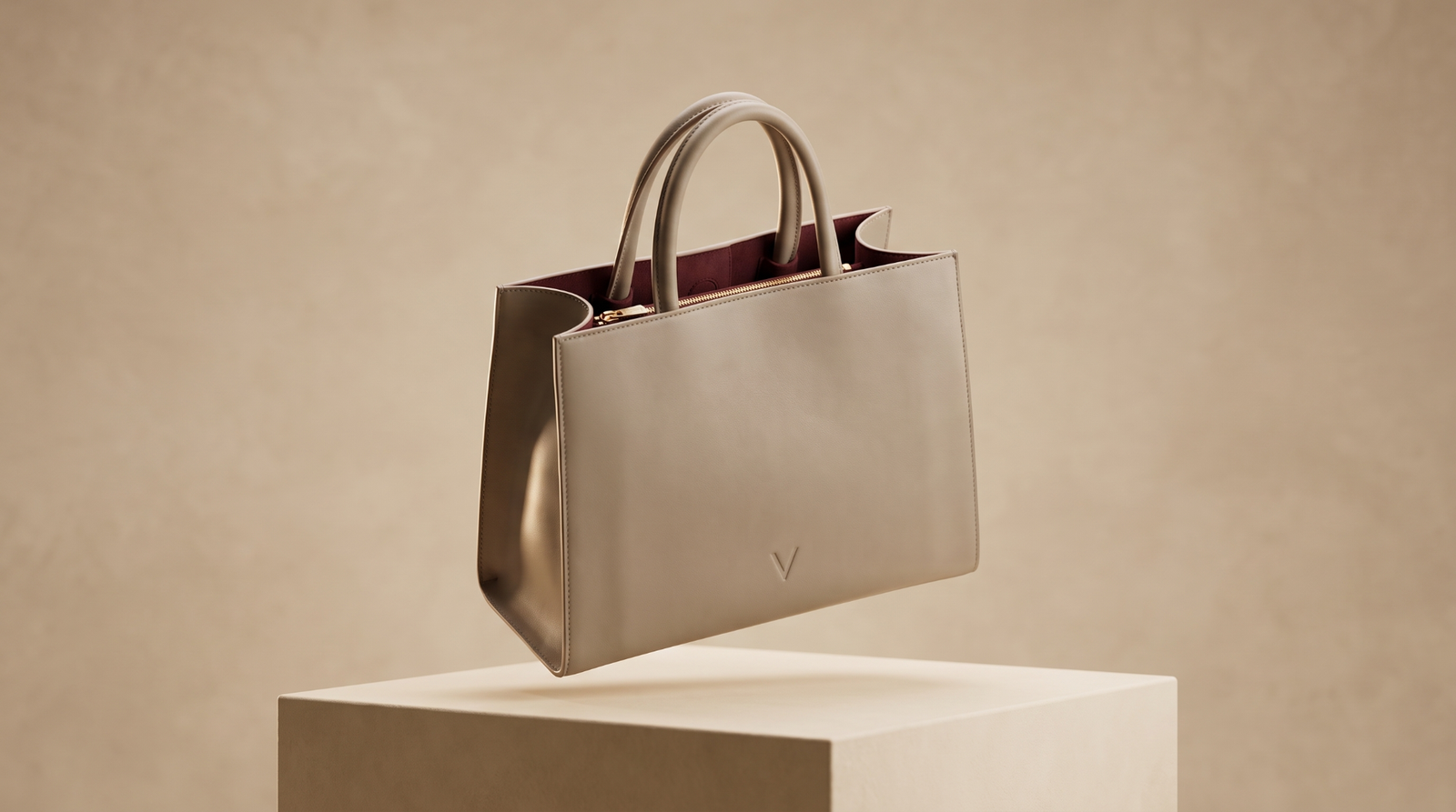 The Véronne Élan tote in taupe top-grain cowhide, suspended above a pale plinth in soft natural light, the dark burgundy suede lining just visible at the opening.